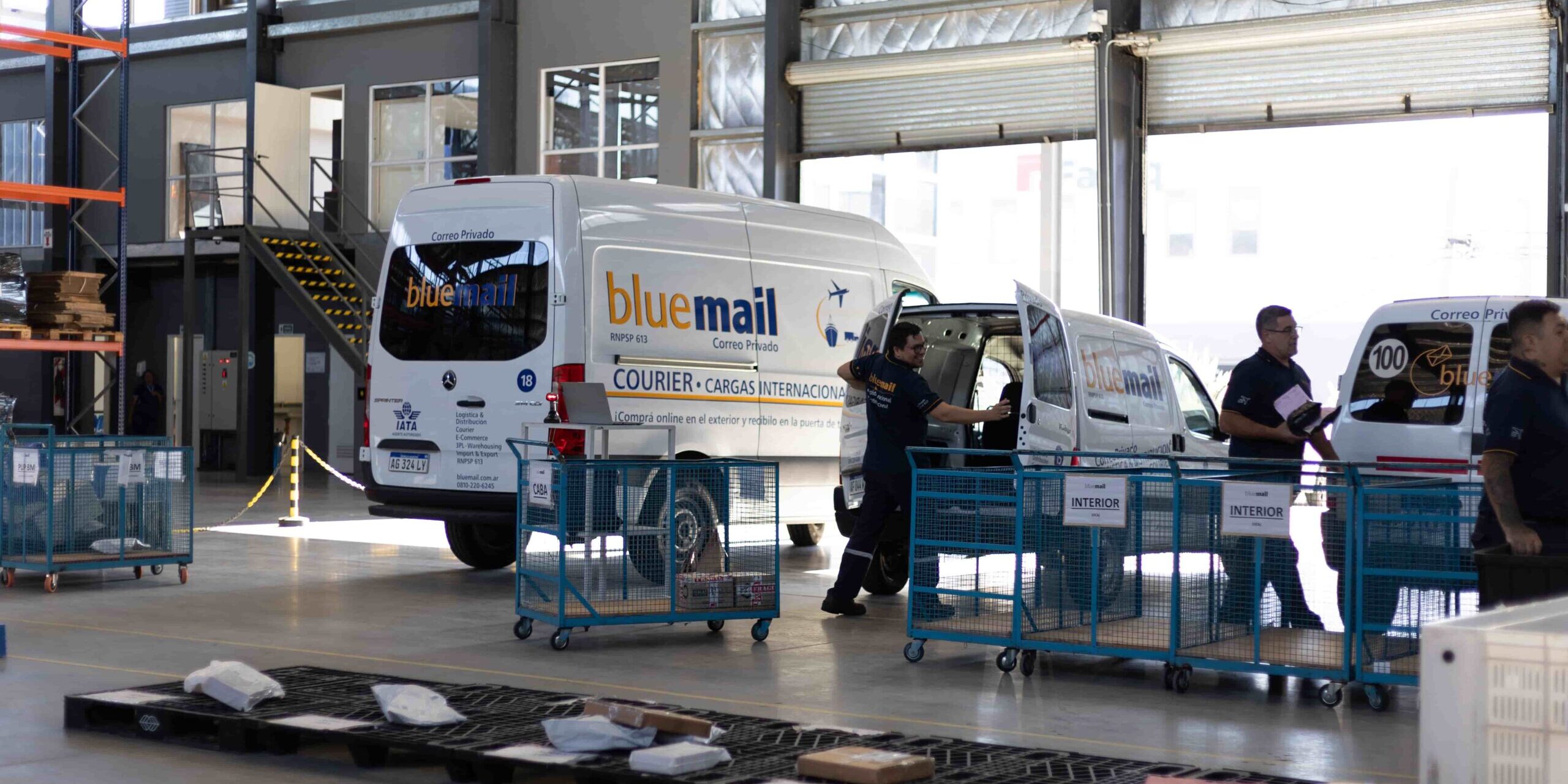 Implementación de ISO 9001 en empresas de logística: operativa del centro logístico de Blue Mail con vehículos y personal gestionando paquetería.