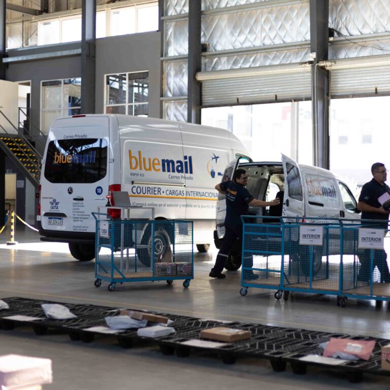 Operativa logística de Blue Mail en centro de distribución Implementación de ISO 9001 en empresas de logística: operativa del centro logístico de Blue Mail con vehículos y personal gestionando paquetería.